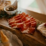Sliced prosciutto on a rustic wooden board with assorted appetizers, perfect for gourmet gatherings.