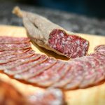 Cold cuts of delicious smoked sausage placed on wooden board amidst sausage slices in kitchen